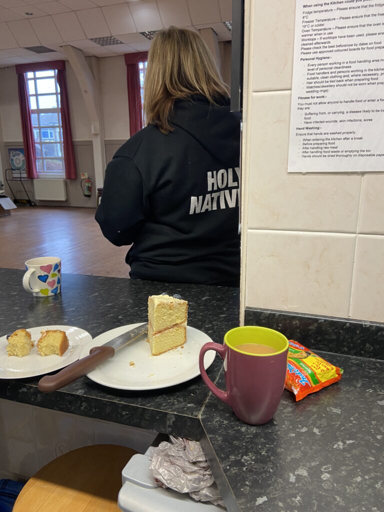Plates of sponge cake and mugs with the back of a volunteer wearing a black hoodie that says holy nativity on the back