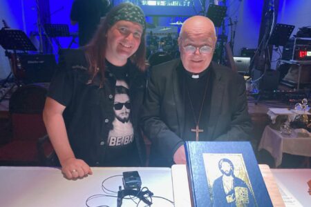 Vicar and Archbishop preparing for the service standing at the altar in front of a projection screen with blue lighting